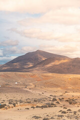 Fototapeta na wymiar Paisaje vertical anaranjado de una paisaje volcánico y rocoso. Cielo niblado y una montaña al fono. (Lanzarote, Islas Canarias, España)