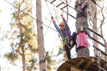 the girl in the orange helmet in the adventure Park holds on to the ropes