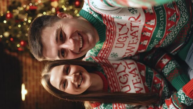 Close up of vertical portrait POV of happy smiling Caucasian married couple in festive mood video chatting on intrnet at home in decorated room on New Year. Merry Christmas concept. Video call online