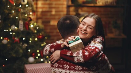 Close up of caucasian family embracing standing near decorated glowing fir tree. Happy wife feels grateful hugs husband express gratitude for New Year gift. Christmas holidays celebration concept