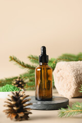 Spa essence oil, pine cones, evergreen branches on beige background. Close up. Vertical format. Winter body and cosmetic care.