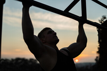 Muscular man doing pullups on sunset sky background. Calisthenics, healthy lifestyle and workout concept 