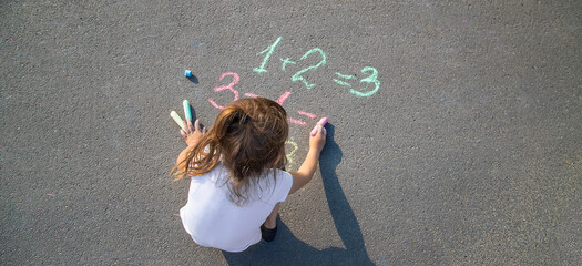 The child solves equations on the asphalt with chalk. Selective focus.