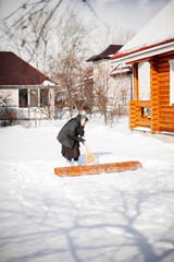 Caucasian woman cleans carpet. Elderly woman in scarf and felt boots sweeps snow from carpet in...