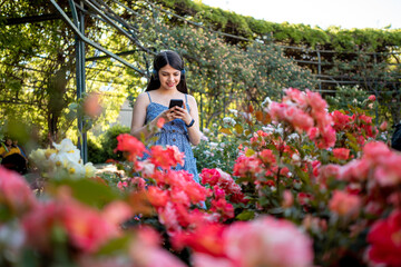 Young woman using a smart phone and headphones at park during spring summer season in vacations