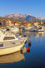 Fototapeta na wymiar Winter Mediterranean landscape.Montenegro. View of Tivat city and Marina Kalimanj for fishing boats and yachts. Snow-capped Lovcen mountain in distance