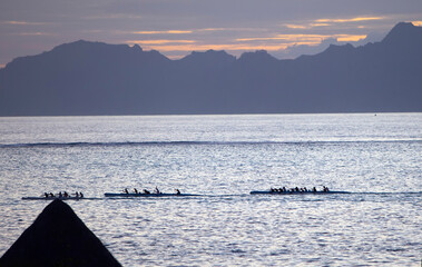 Tahiti. Silhouettes of boats with rowers at sunset in the sea
