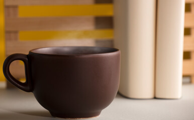 Brown cup of coffee or tea with hot steam, on the table, with books, glasses and brown background.