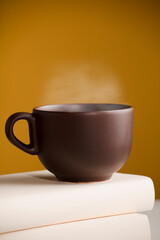 Brown cup of coffee or tea with hot steam, on the table, with books