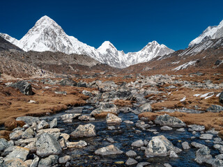 Fototapeta na wymiar view to mountain creek and view to triangle summit Pumori under blue sky in Nepal