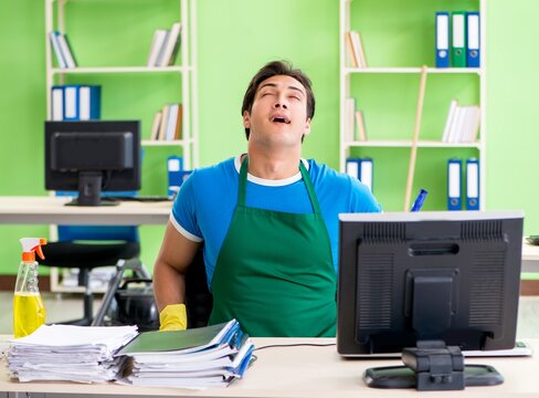 Handsome man cleaning office with vacuum cleaner