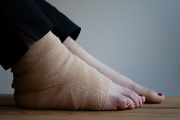 Close up of feet of a person. One foot wrapped with elastic bandage due after injury.