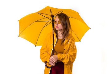 A girl in a yellow raincoat and glasses stands under an umbrella. Isolate on white background