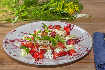 A salad of strawberries, herbs and vegetables is on a plate