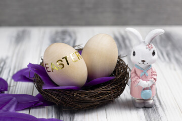 Easter bunny with a nest for eggs and with purple scattered feathers on a white wooden background. Concept for the Christian Easter holiday.
