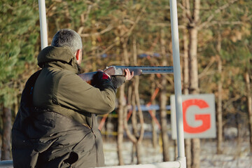 Naklejka premium Hunter in camouflage with rifle in winter forest. Hunt concept. Man securing a reserve, on a snowy day. Hunter takes aim from a gun in the snowy forest