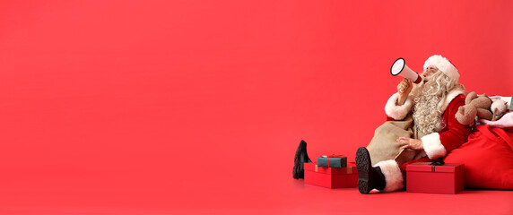 Santa Claus with megaphone, bag and gifts on red background with space for text