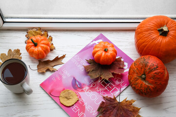 Cup of coffee with magazine and pumpkins on windowsill