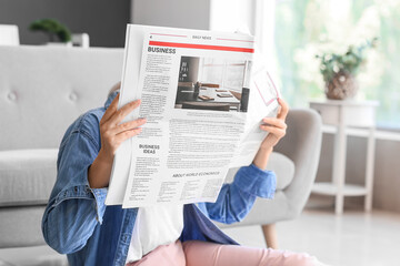 Mature woman reading newspaper on floor at home