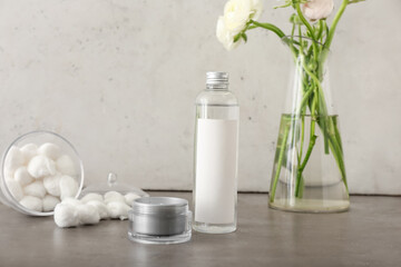Fototapeta na wymiar Bottle with cosmetics, jar with face cream and vase with ranunculus flowers on grey table