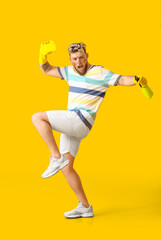 Fototapeta na wymiar Dirty young man with cleaning sponge and detergent on yellow background