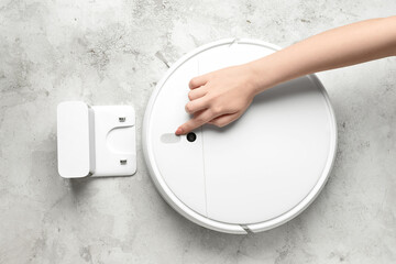 Female hand with modern robot vacuum cleaner on grunge background