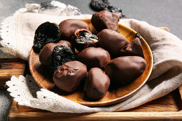 Delicious chocolate candies with prunes in plate on wooden board, closeup