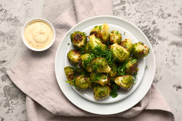 Plate with tasty roasted Brussels cabbage and sauce on color background