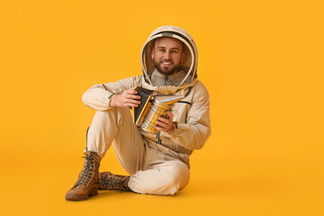 Male beekeeper in protective suit with smoker on yellow background