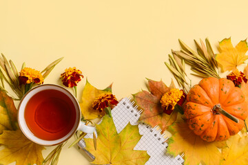 Cup of tea with notebook, pumpkin and fallen leaves on beige background