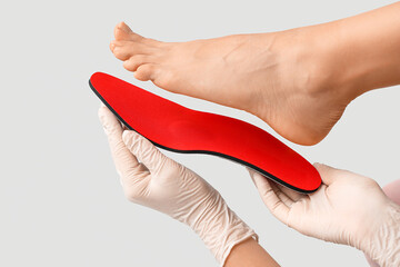 Orthopedist with red insole and female foot on light background, closeup - obrazy, fototapety, plakaty