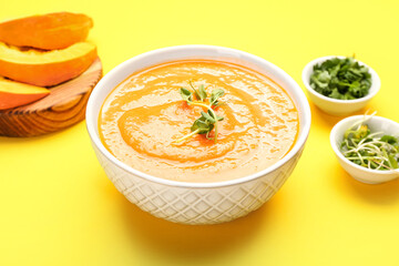 Bowl of delicious pumpkin cream soup on yellow background