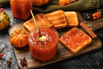 Bowl of sweet pumpkin jam with toasts on black background