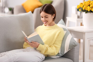 Beautiful young woman reading book on sofa at home