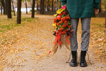 Young woman wearing boots with untied shoelaces and holding bouquet in autumn park