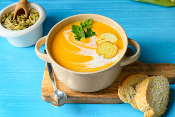 Pot with delicious pumpkin cream soup, seeds and croutons on color wooden background