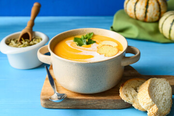 Pot with delicious pumpkin cream soup, seeds and bread on color wooden background, closeup