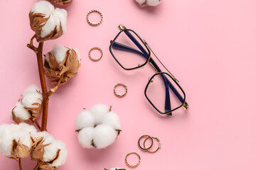 Branch of beautiful cotton flowers, eyeglasses and stylish jewelry on color background, closeup