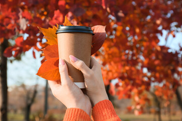 Woman holding fallen leaves and paper cup of coffee in autumn park