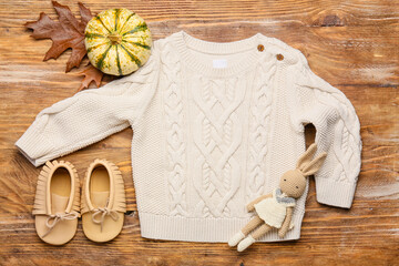 Stylish baby sweater, toy, shoes and pumpkin on wooden background