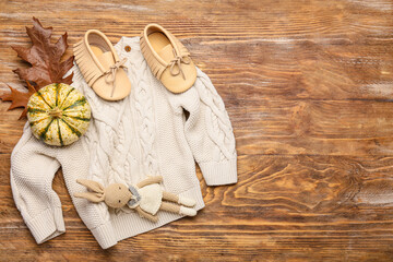 Stylish baby sweater, toy, shoes and pumpkin on wooden background