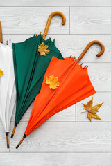 Different umbrellas and autumn leaves on light wooden background