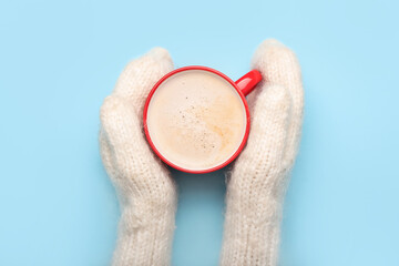 Female hands in knitted mittens and cup of tasty cacao on color background, closeup
