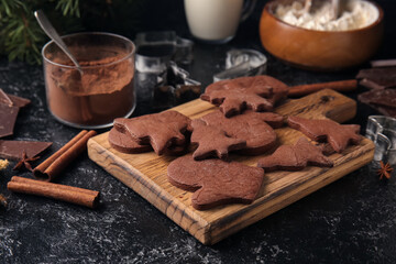 Wooden board with tasty chocolate Christmas cookies on black background