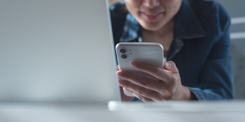 Close up of young asian business woman using mobile phone making video call via online meeting app during working on laptop computer from home office.