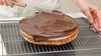 Woman topping cake with chocolate glaze. Chocolate cake close up on cooling  rack on kitchen table. Step by step baking process