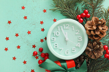 Stylish alarm clock, fir branches and Christmas decor on green background