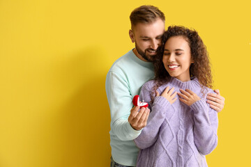 Young man proposing to his girlfriend on color background
