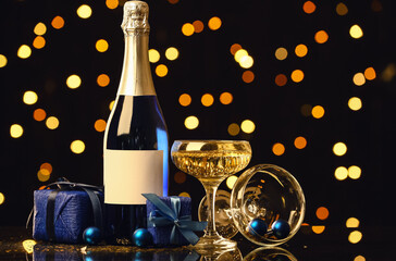 Bottle and glass of champagne with Christmas gift boxes on table against blurred background