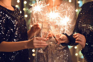 Women in elegant dresses with Christmas lights and glasses of champagne, closeup